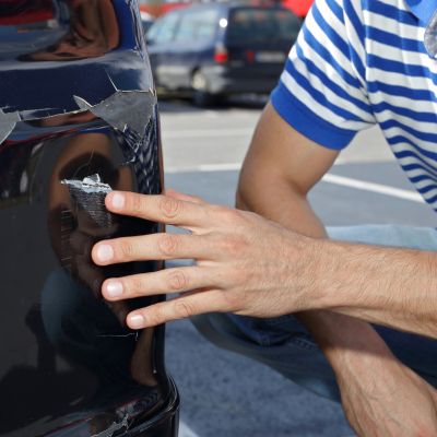 Car damaged in parking lot. Man checking car scratches and dents (Demo)